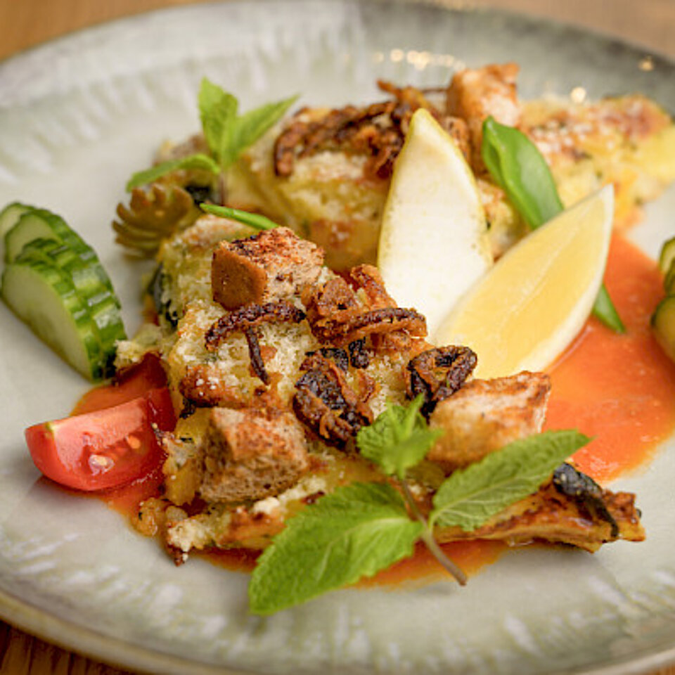 Ein Teller mit einem Gericht aus gebackenem Fisch, garniert mit Zitronenspalten, Tomatenstücken, Gurkenscheiben, frischen Kräutern und einer roten Sauce.
